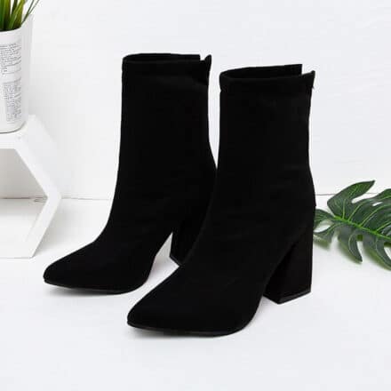 Bottes noires à talons avec zip à l'arrière et bouts pointus. Feuille de plante en arrière plan.