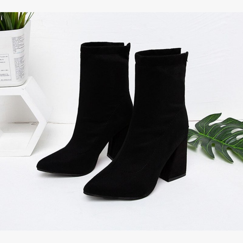 Bottes noires à talons avec zip à l'arrière et bouts pointus. Feuille de plante en arrière plan.