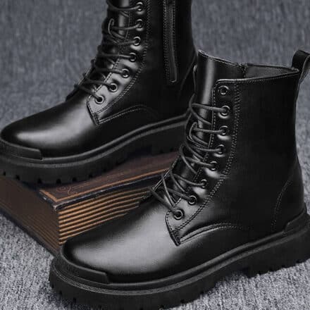 Bottes mi-hautes noires à lacets un sur un livre ancien l'autre a terre sur un sol gris