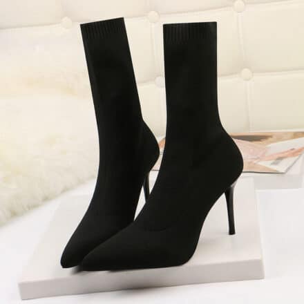 Bottes chaussettes a talons hauts noir sur une plateforme de quelque centimètre blanc sur un mur en brique blanc