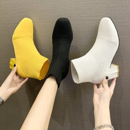 Paires de 3 bottes blanche, noir et jaunne dont 2 en main et une porté a un pied sur un fond gris