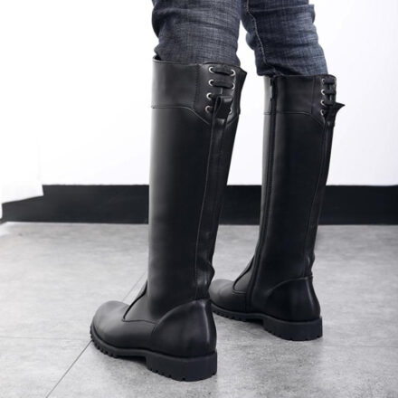 Bottes d'équitation noires avec des lacets portées par un personne avec un jean sur un carrelage gris