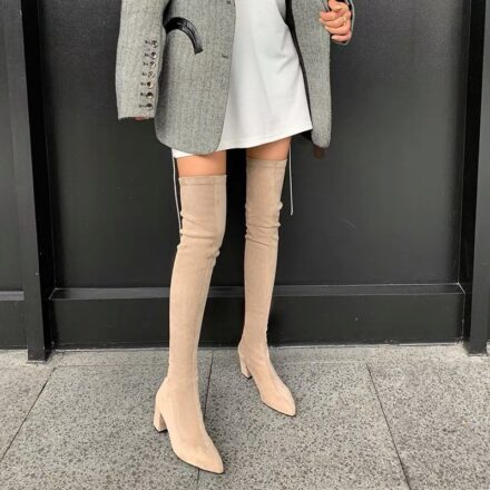 On voit les jambes d'une femme qui portent des bottes cuissardes en daim beige. Elle a également une robe et manteau mais on voit seulement ses jambes.