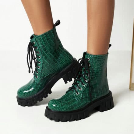 Paire de bottes mi haute à lacets. Elles sont vertes en imprimé crocodile et portées par une personne dont on voit seulement les mollets.