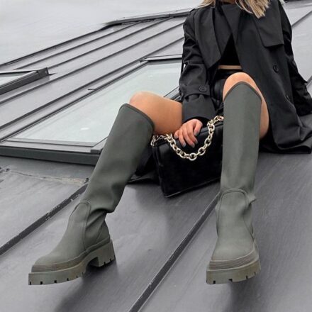 Bottes grises hautes pour femme en caoutchouc tendance pour femme. Fille assise, blouse noire, bottes grises, et sac noir à chaine.