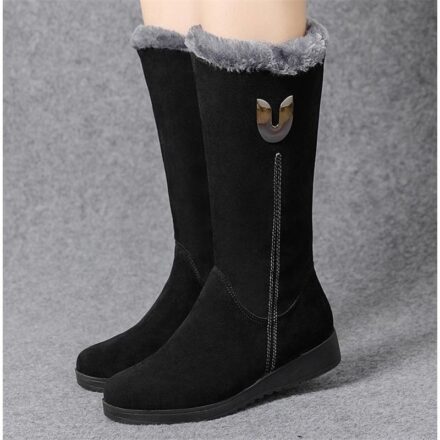 Bottes fourrées plates noires, jambes de femme, sur fond gris