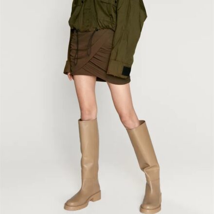 Bottes marron porté par une femme en jupe marron et haut vert sur un fond blanc