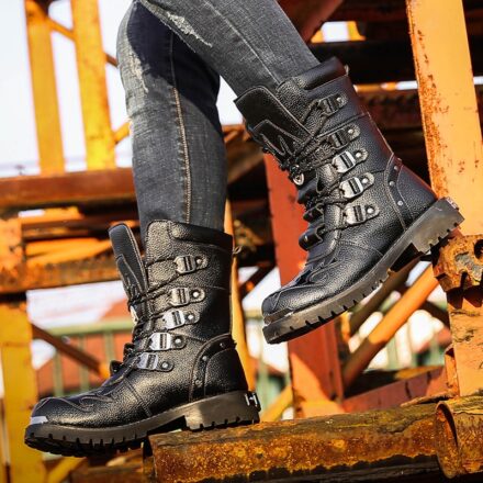 Bottes noire larges portées par un hommes en jean noir sur une structure rouillée