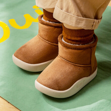 On voit des pieds d'enfants, de bébé, avec des bottes de neige camel à la semelle en caoutchouc blanc.