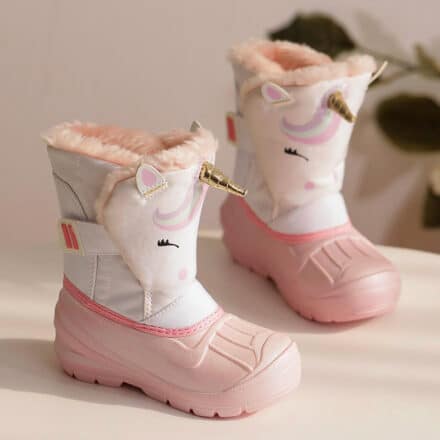 Bottes motif licorne bas de la bottes rose et haut blanc sur une table en bois claire avec un fond rose clair et une plante verte en fond