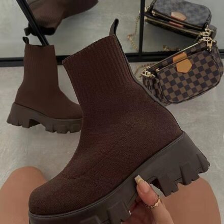 Botte chaussette marron tenu par une femme devant un miroir avec l'autre paire au sol blanc à coté d'un sac a main