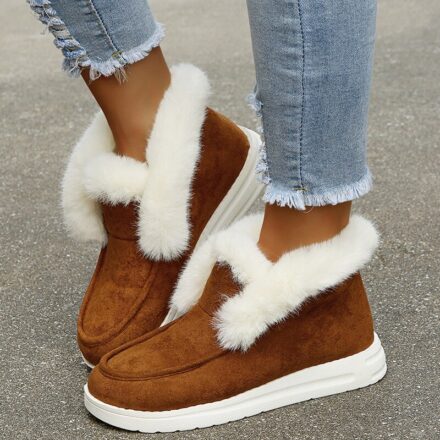 On voit les pieds d'une jeune femme qui porte un jean au bas déchiré et des bottines fourrées en fourrure marron. elles ont l'air très chaudes et confortables.