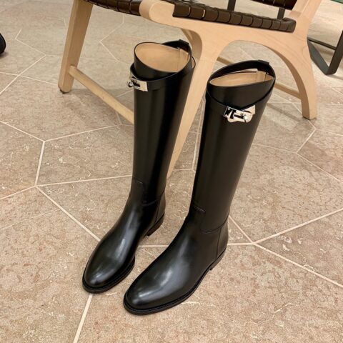 paire de botte noire d'été avec boucle dorée posées aux pieds d'une chaise en bois, sur du carrelage, elles ne sont pas portées
