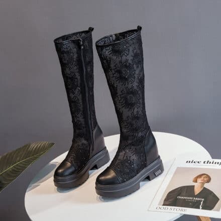 posées sur une table ronde blanche, une paire de bottes noires en dentelle aux motifs à fleurs et semelle compensée, elles sont près d'un magazine