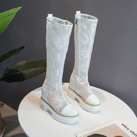 posées sur un table ronde blanches, une paire de bottes blanche en dentelle aux motif à fleurs et semelle compensée