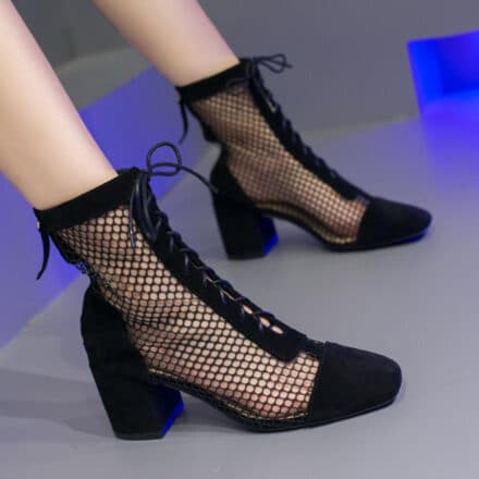 Paire de bottes noires d'été basses en maille portées par une femme dont on ne voit que les jambes , à lacets sur le devant et fermeture éclaire à l'arrière, les pieds sont posés au sol à plat