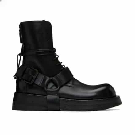 Bottes noire mi-haute à lacets, à bout rond, à plateforme avec une grosse sangle décorative qui passe sous la semelle et autour de la cheville. De profil sur fond blanc.